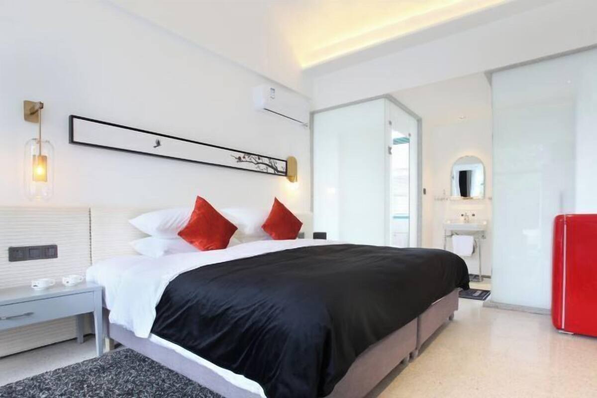 A modern hotel room with a large bed, a bedside table, a red cabinet, and a bathroom visible through an open door.