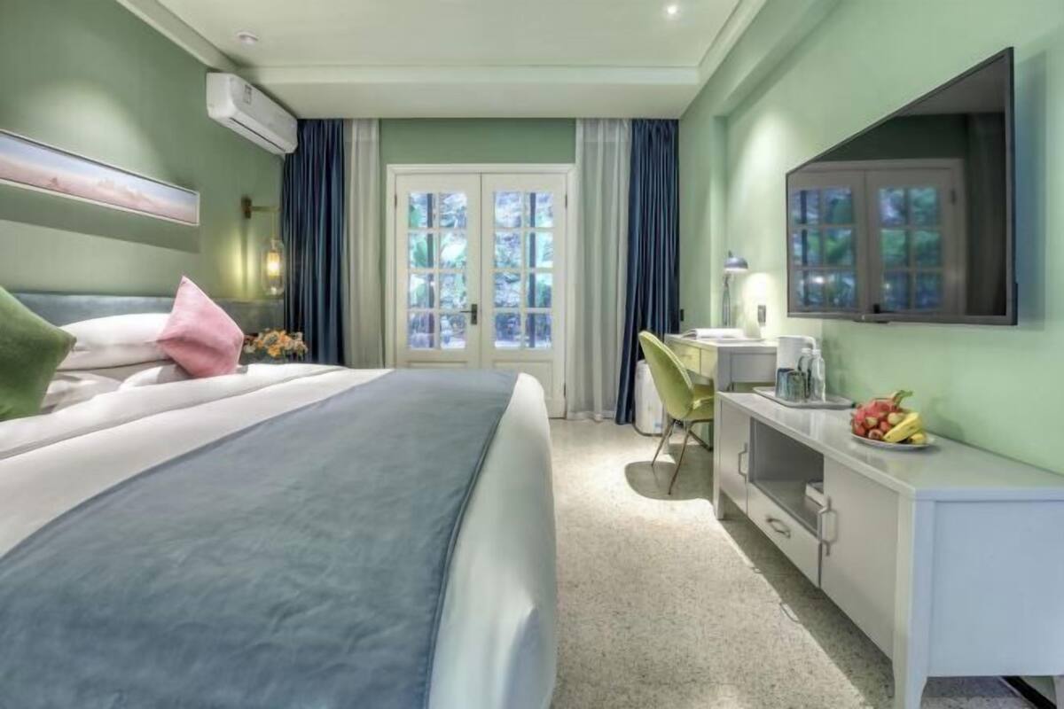 A hotel room with a bed, a desk, a chair, a TV, and a window with curtains.
