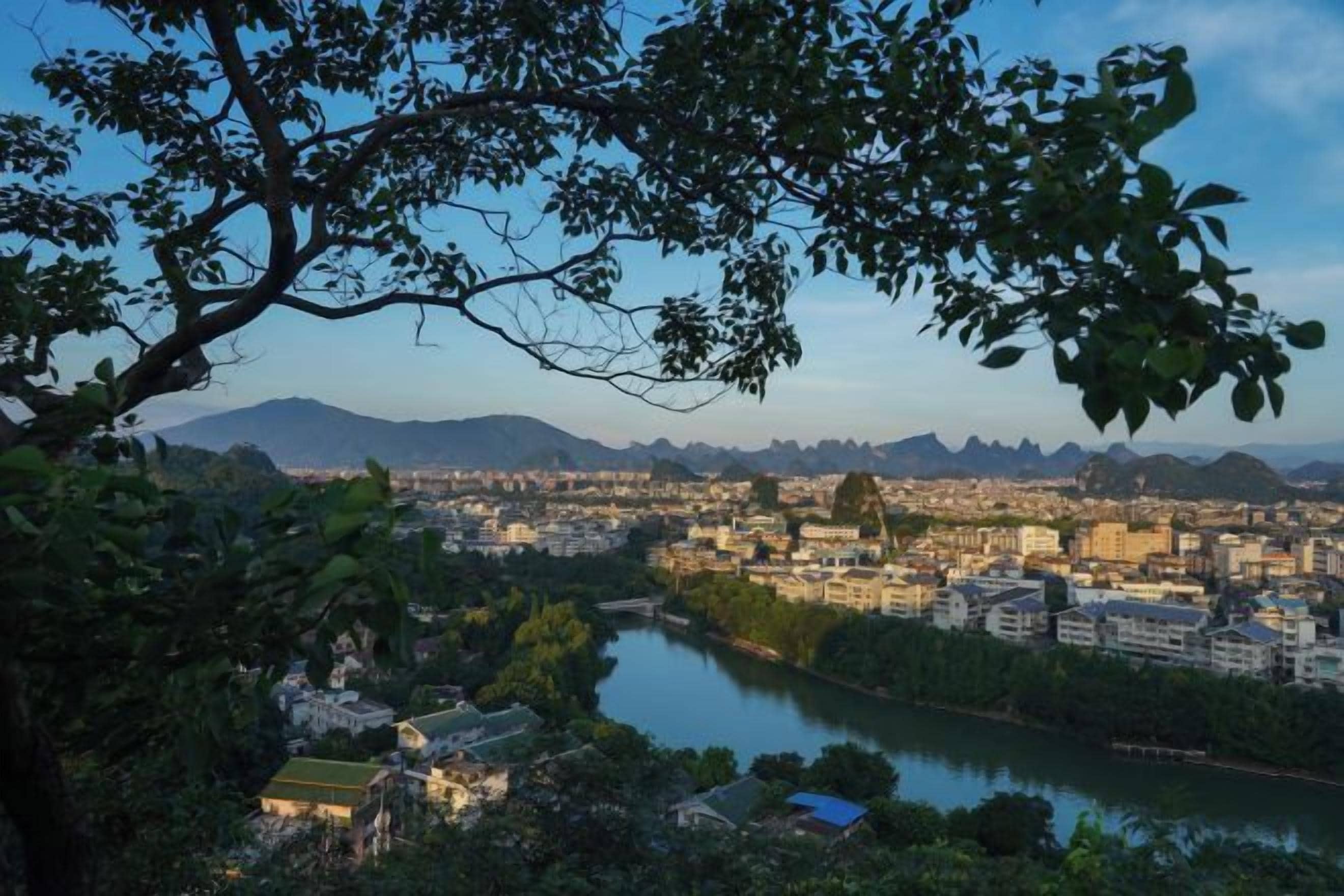 A cityscape with a river, buildings, and mountains in the background.