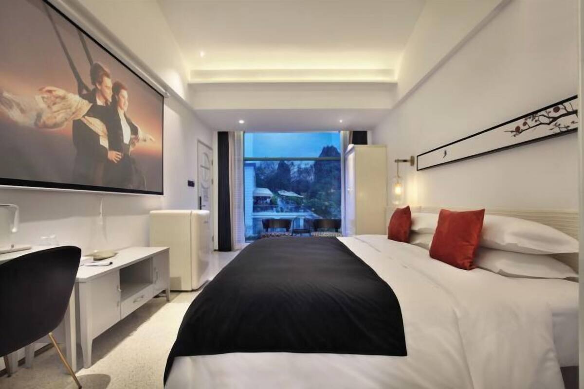 A modern hotel room with a large bed, a desk, a television, and a view of the outdoors.