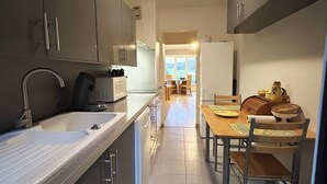 Une cuisine étroite avec un évier, une cuisinière et des placards. On aperçoit à l’arrière-plan un coin repas avec une table et des chaises.