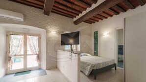 A bedroom with a bed, a TV, a bathroom, and a door with curtains.