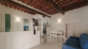A spacious living area with a dining set, a blue sofa, and a kitchen in the background.