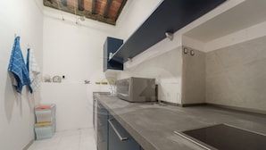 A modern kitchen with a stainless steel sink, a microwave, and a built-in oven. There is a small trash bin and a towel rack with blue towels.