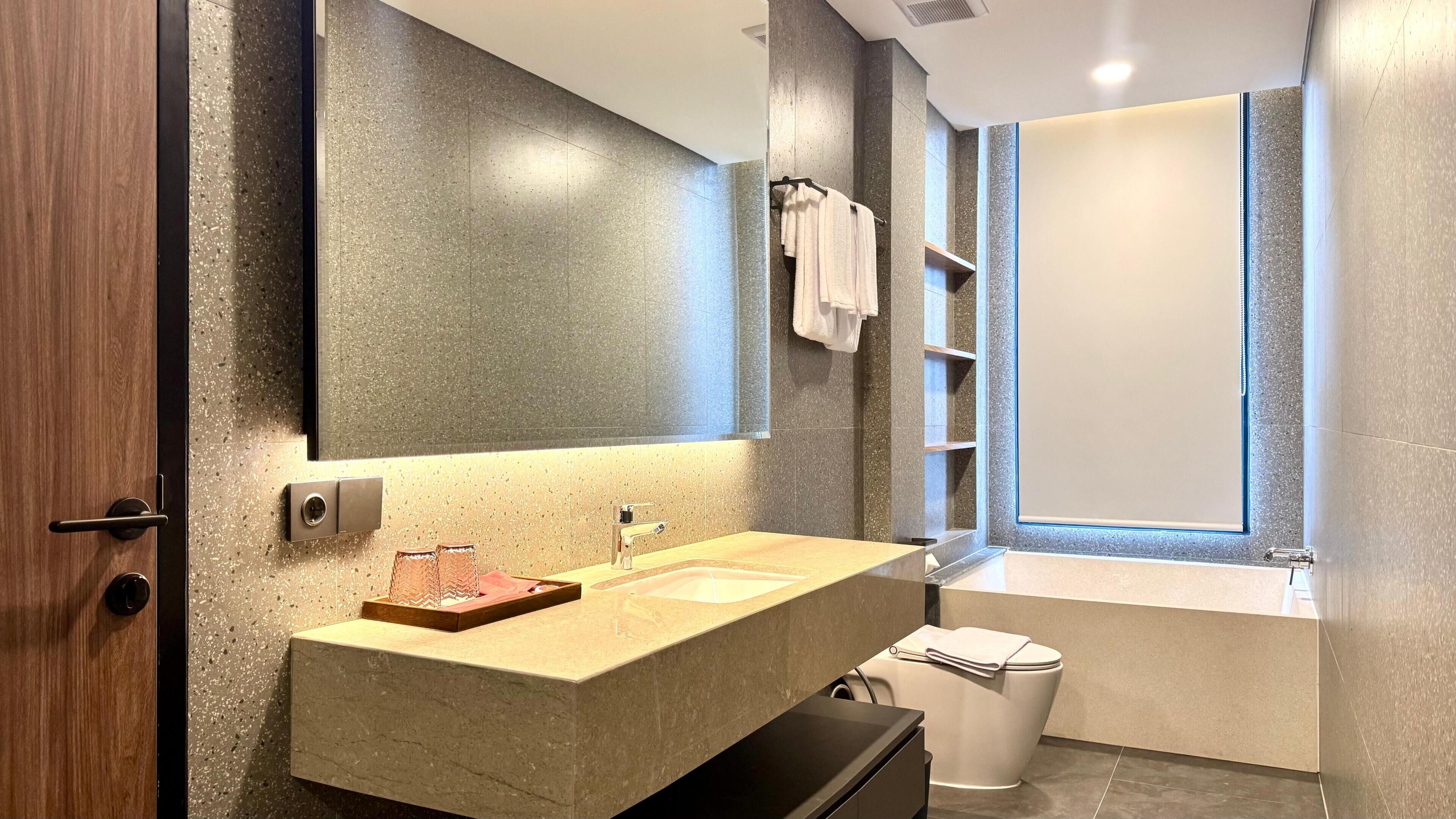 Un baño moderno con encimera de granito, un espejo grande, un perchero y un inodoro.