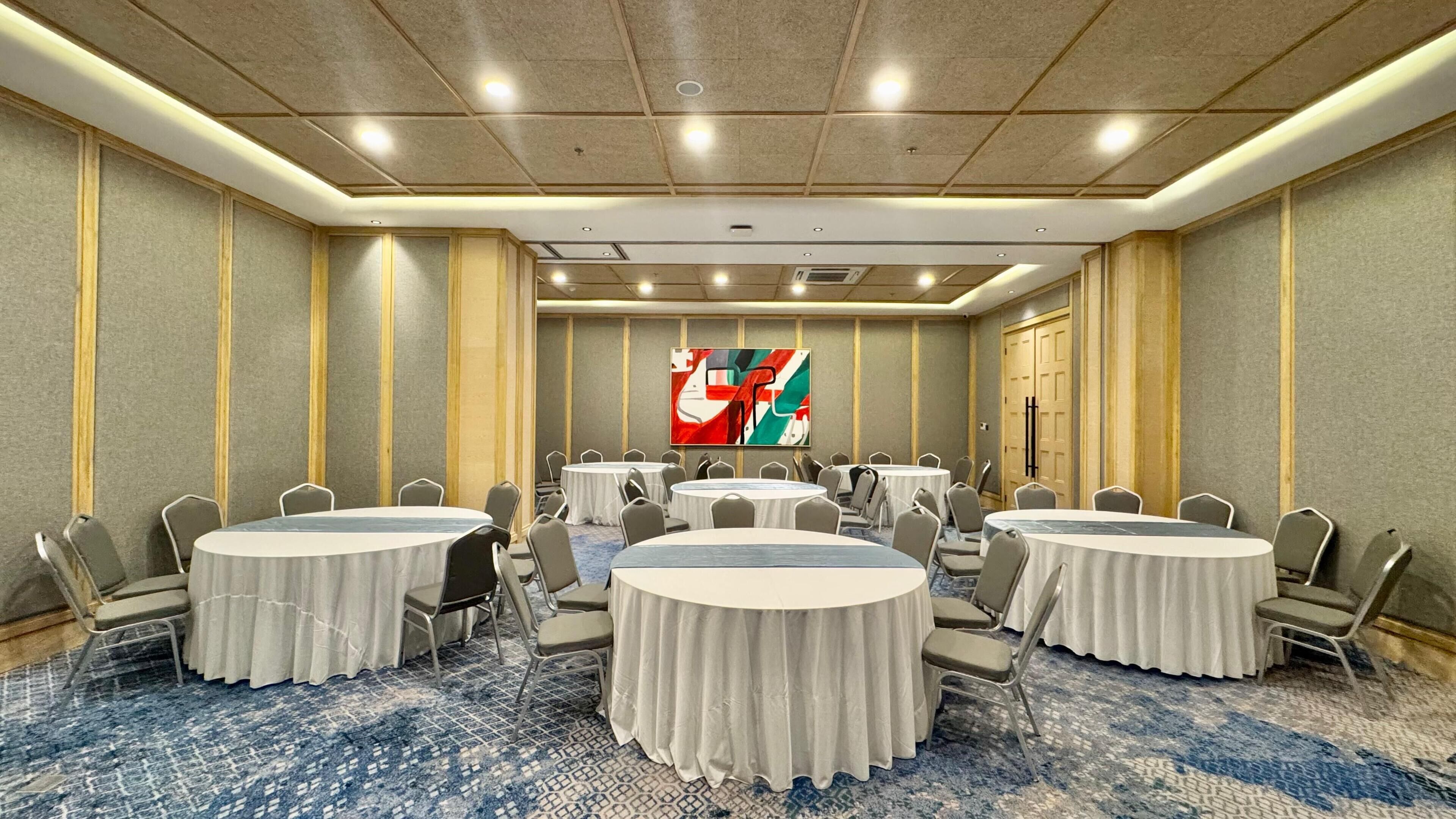 A conference room with round tables, chairs, and a large abstract painting on the wall.