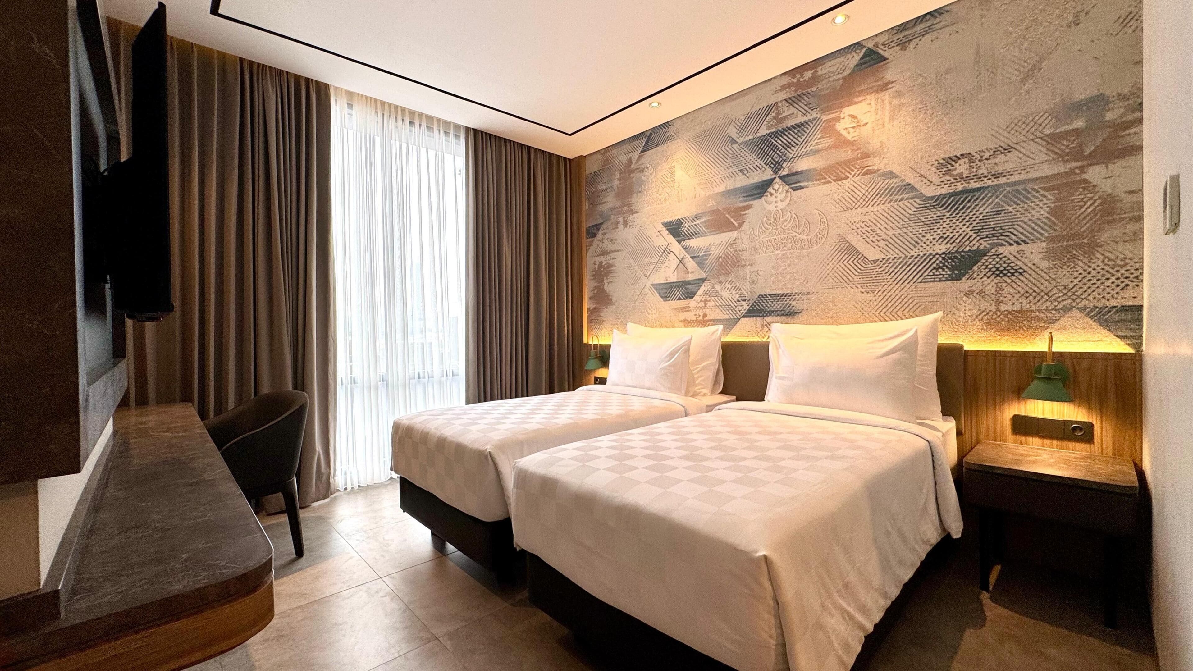 Habitación de hotel con dos camas, televisión, escritorio y pared con diseño.