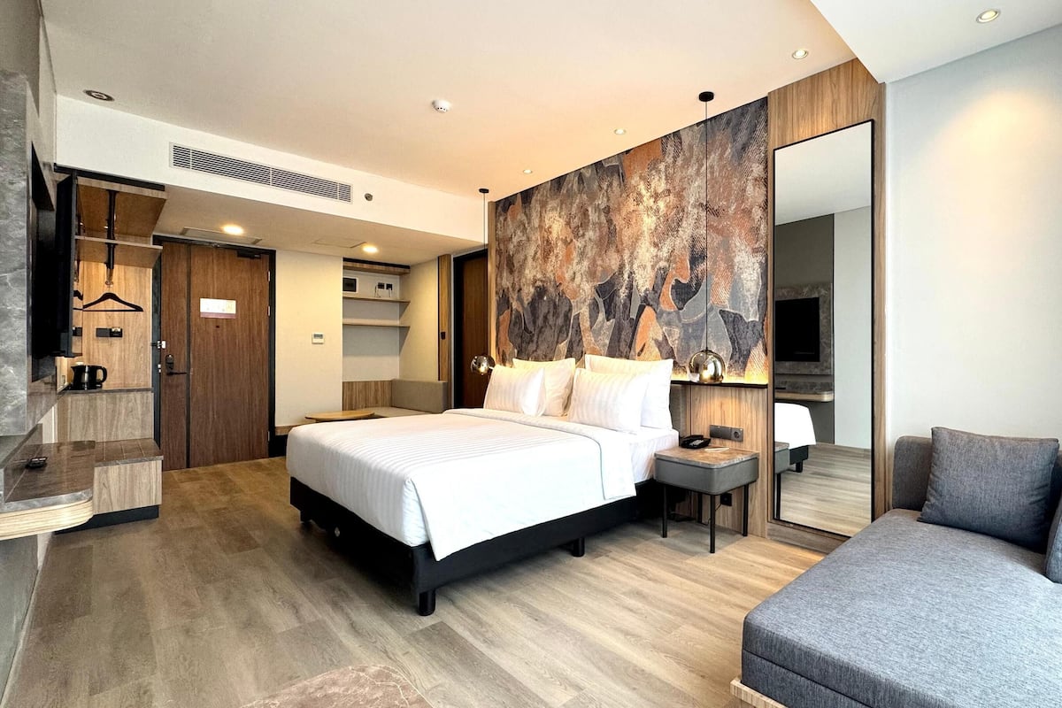 Een moderne hotelkamer met een groot bed, nachtkastje en een zithoek met een bank.