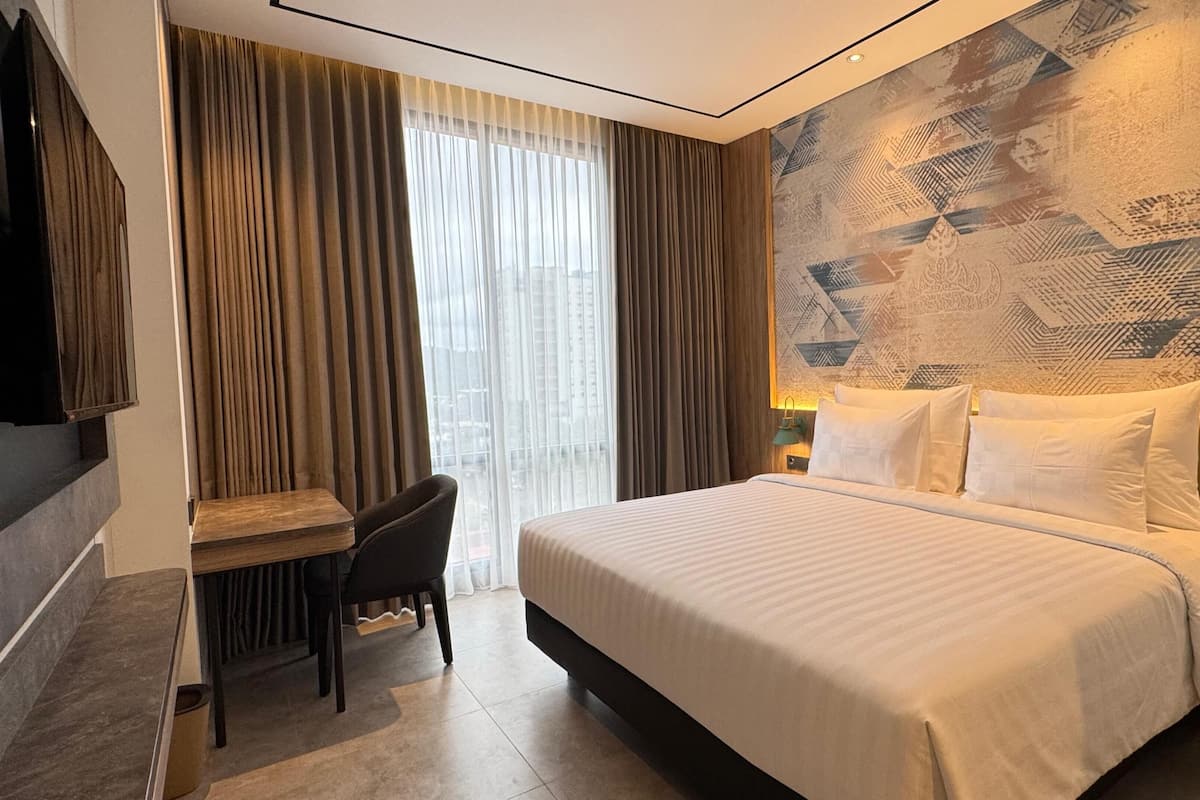 Een hotelkamer met een bed, een bureau, een stoel, een televisie en een behang met patroon.