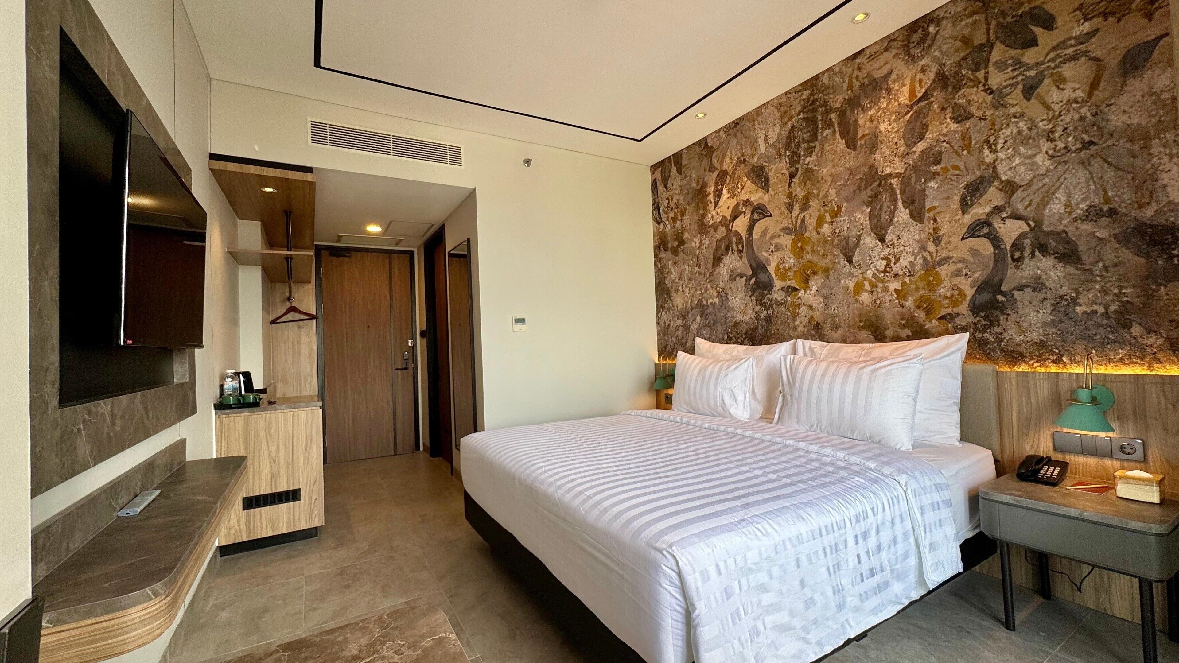 Een moderne hotelkamer met een groot bed, een flatscreen televisie aan de muur, een houten dressoir en een decoratief muurschildering.