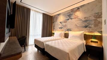 A hotel room with two beds, a desk, a chair, a TV, and a patterned wall.