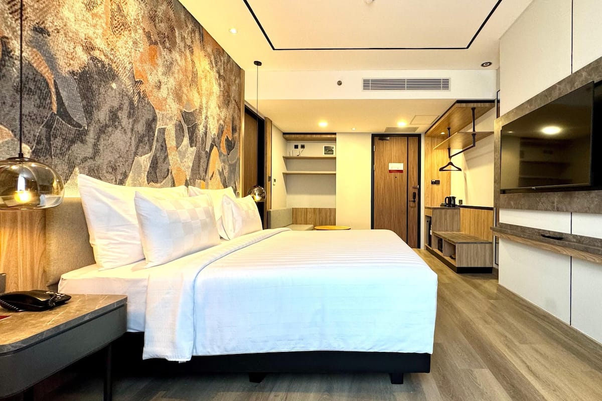 Een moderne hotelkamer met een groot bed, een flatscreen televisie aan de muur, een houten bankje en een groot abstract schilderij.