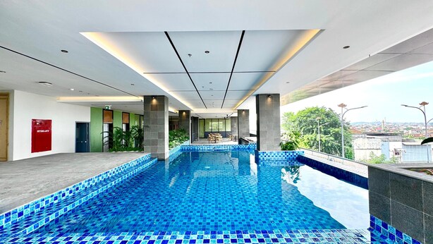 A modern indoor swimming pool with a tiled floor, a seating area with tables and chairs, and a view of the cityscape.