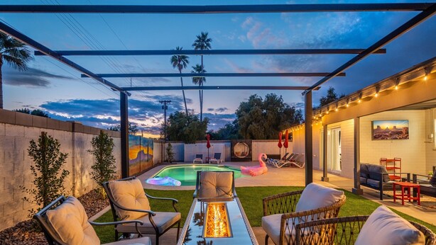 Ein Garten mit Feuerstelle, Liegestühlen, Pool und einer überdachten Terrasse.