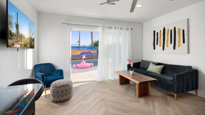 Ein modernes Wohnzimmer mit Deckenventilator, Flachbildfernseher, blauem Sessel, Holztisch und dunkler Couch.
