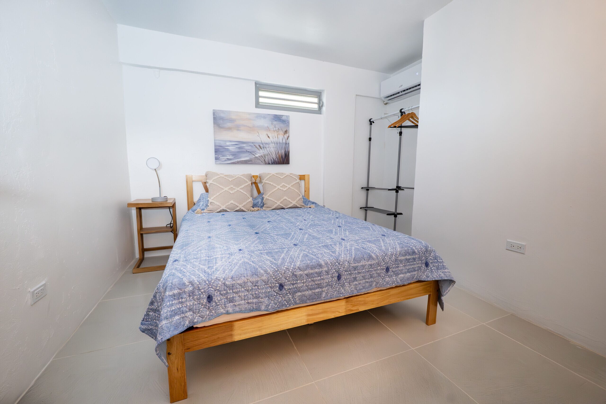 A bedroom with a wooden bed, a bedside table, a hanging light, and a wall-mounted air conditioning unit.