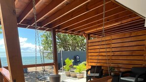 An outdoor patio with a wooden swing, seating area, and a view of the ocean. - Oceanfront Retreat w/ Terrace, Direct access to Beach & BBQ (Mayaguez)