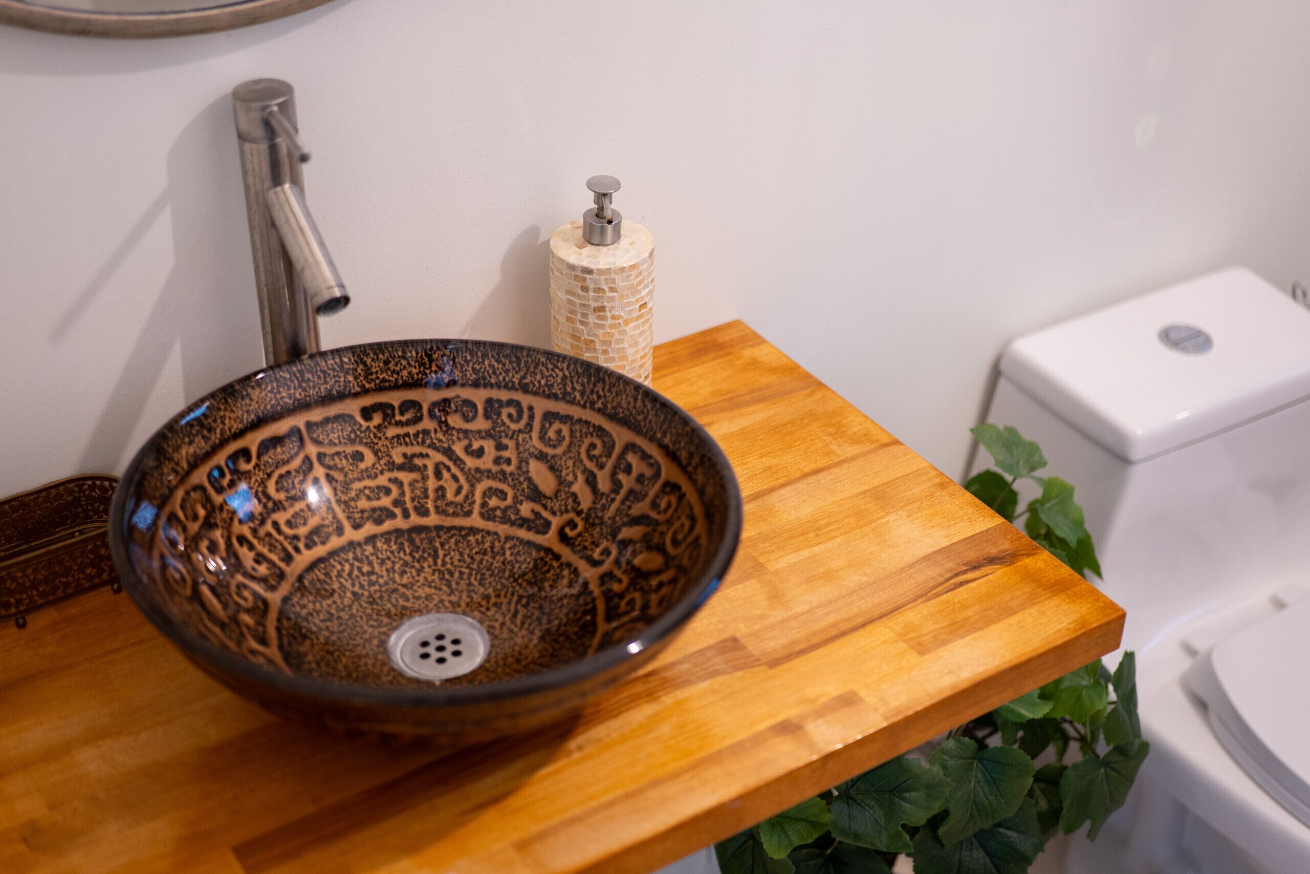 Une salle de bain avec un lavabo en céramique, un plan de toilette en bois, des toilettes et un distributeur de savon fixé au mur.