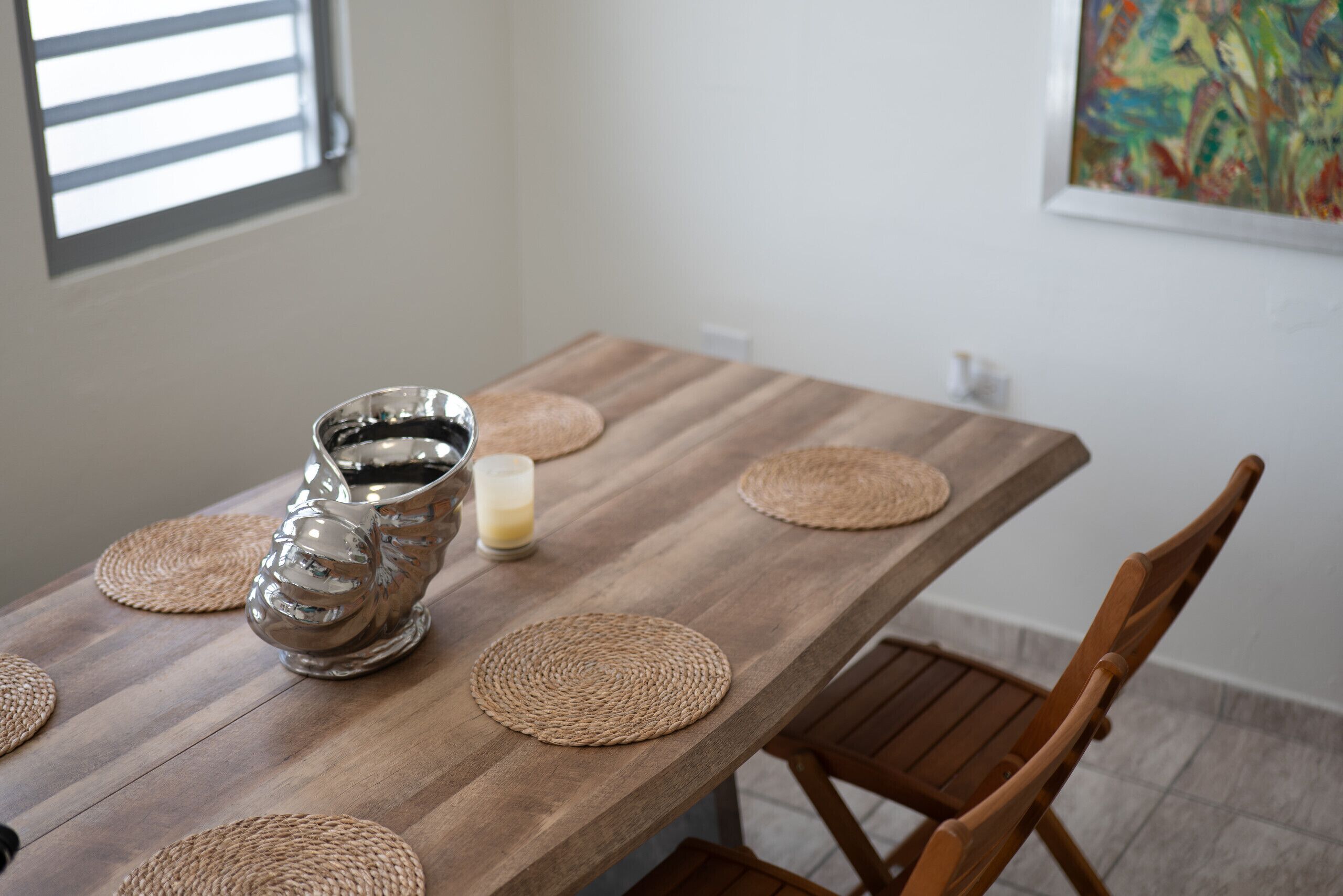 Una mesa de madera con individuales tejidos, una jarrón de plata y una vela.