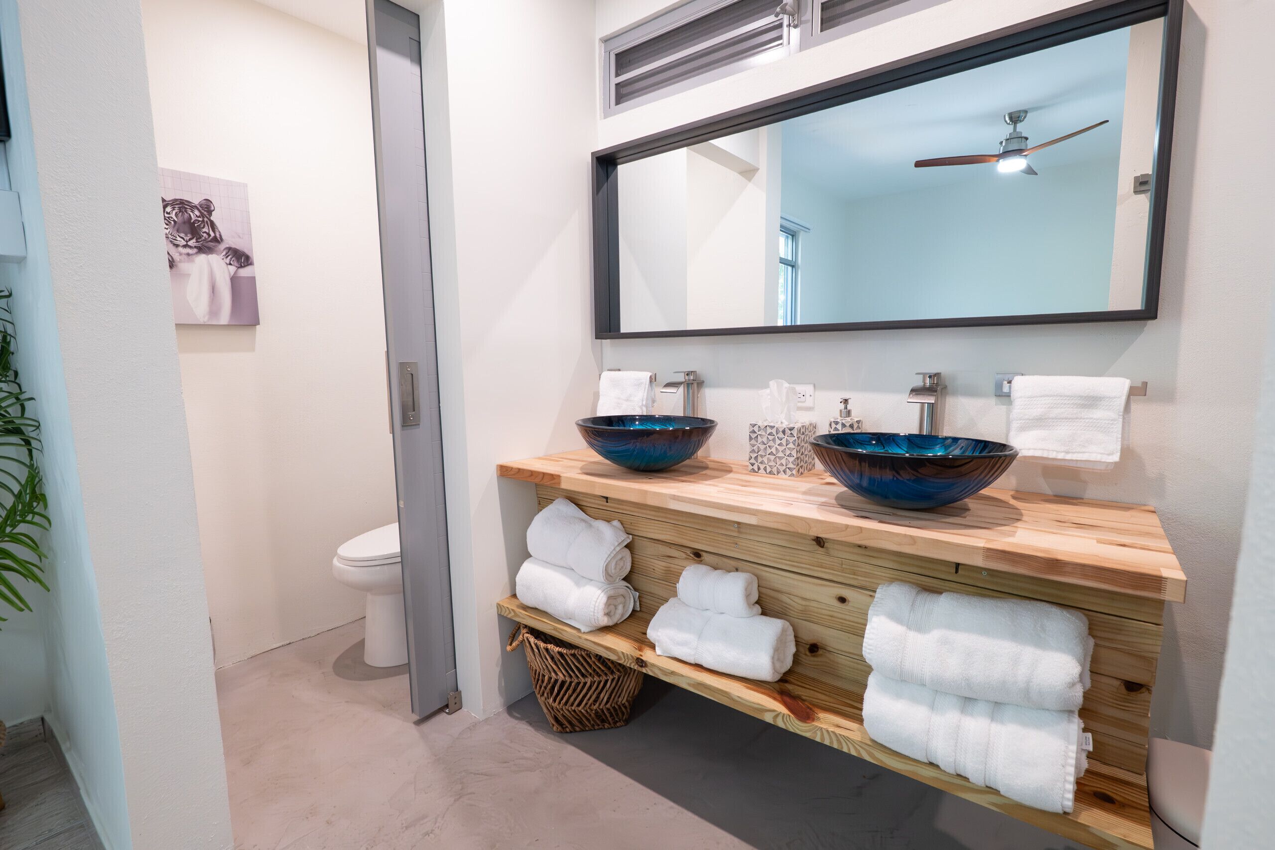 A modern bathroom with two large blue bowls, a wooden vanity, and a ceiling fan.