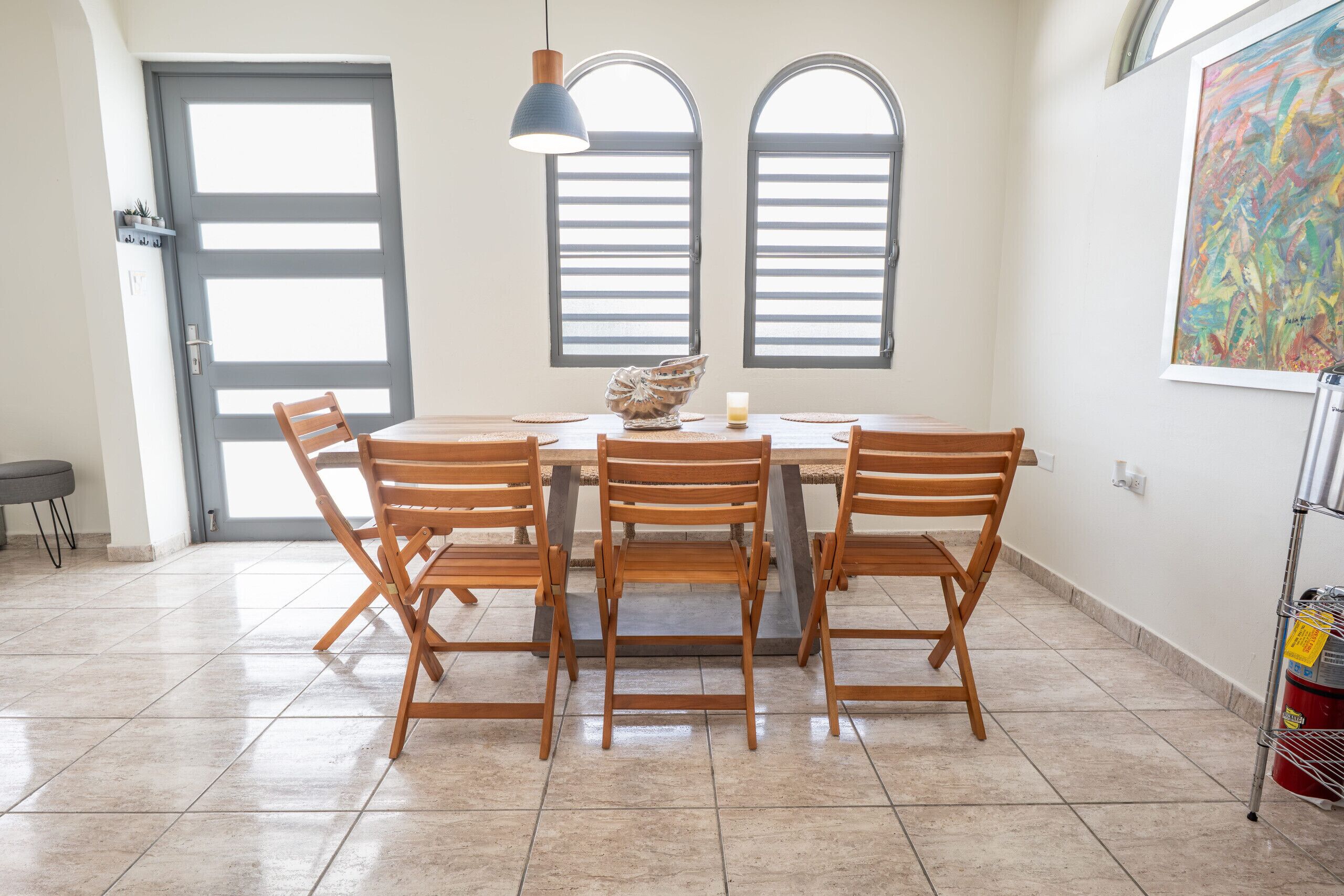 Un coin repas comprenant une table ronde, quatre chaises en bois, un vase décoratif et deux fenêtres en arc de cercle.