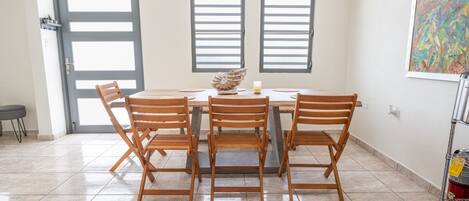 Un coin repas comprenant une table ronde, quatre chaises en bois, un vase décoratif et deux fenêtres en arc de cercle.