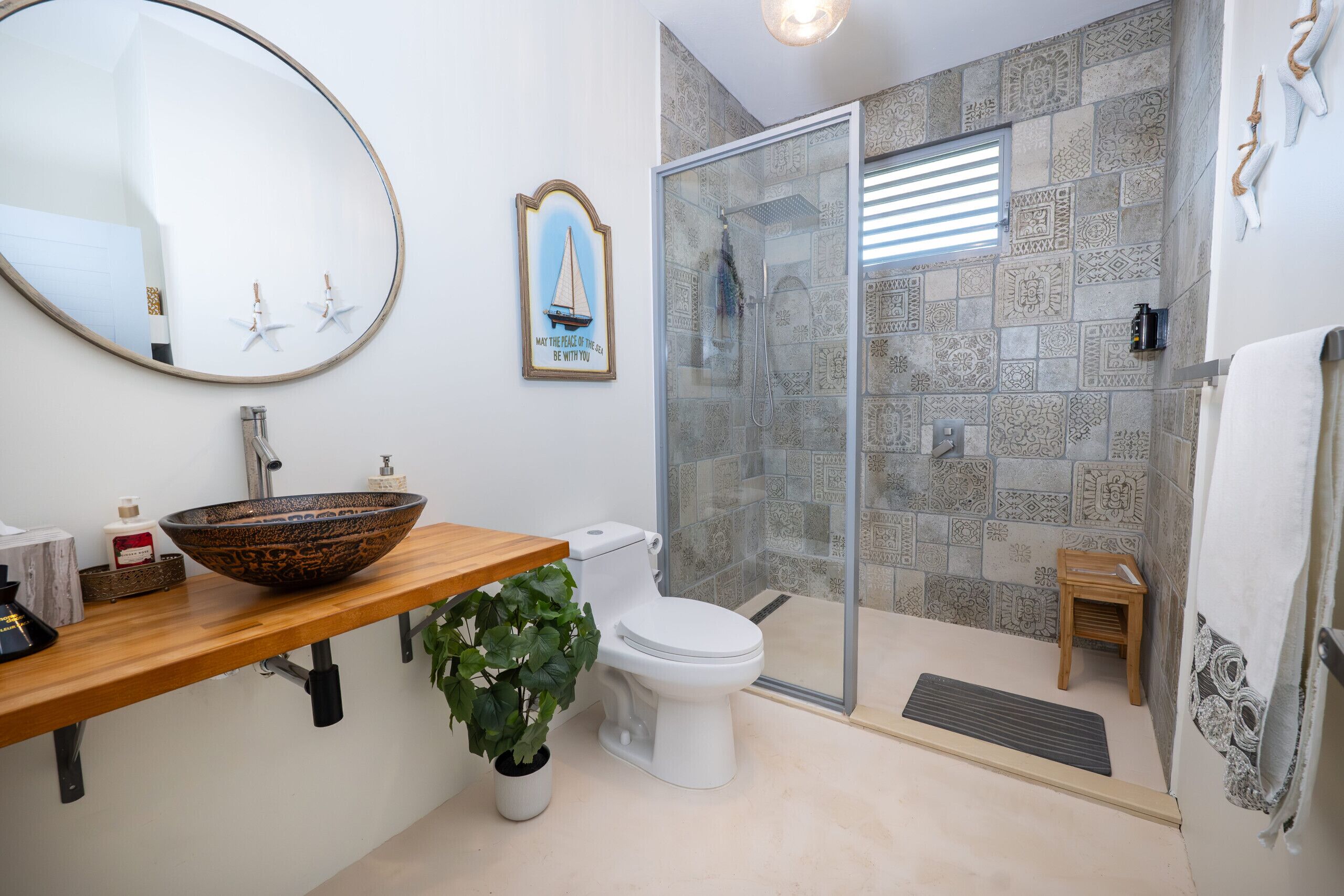 A bathroom with a wooden vanity, a large mirror, a white toilet, a glass-enclosed shower, and patterned tiles.