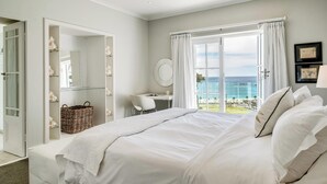 A bedroom with a bed, a desk, a chair, a large window with a view of the ocean, and a wardrobe with shelves. - Incredible 6bed w Pool in Camps Bay Villa Galazzio (Cape Town)
