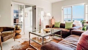 A living room with a glass coffee table, leather sofas, a wooden chair, and a view of the sea. - Incredible 6bed w Pool in Camps Bay Villa Galazzio (Cape Town)