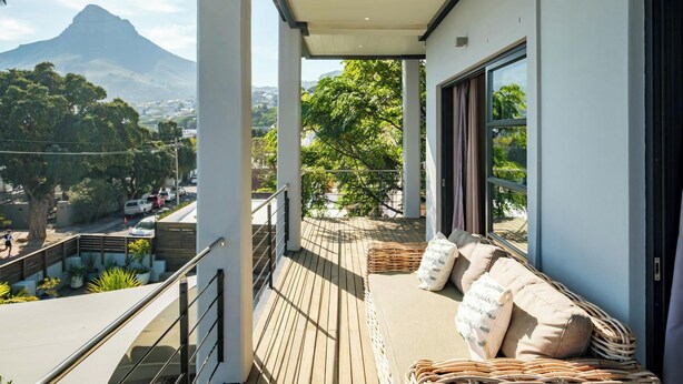Un balcón con vista a la montaña, muebles de mimbre y una barandilla.