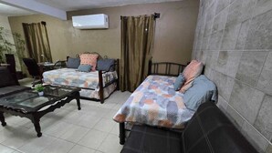 Habitació amb dos llits, un sofà, una taula de café amb superfície de vidre i aire condicionat fixat a la paret.