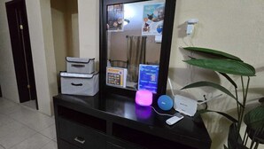 Habitació d'hotel amb un taulell negre, un mirall, una planta, una làmpada rosa, un altaveu i un router.