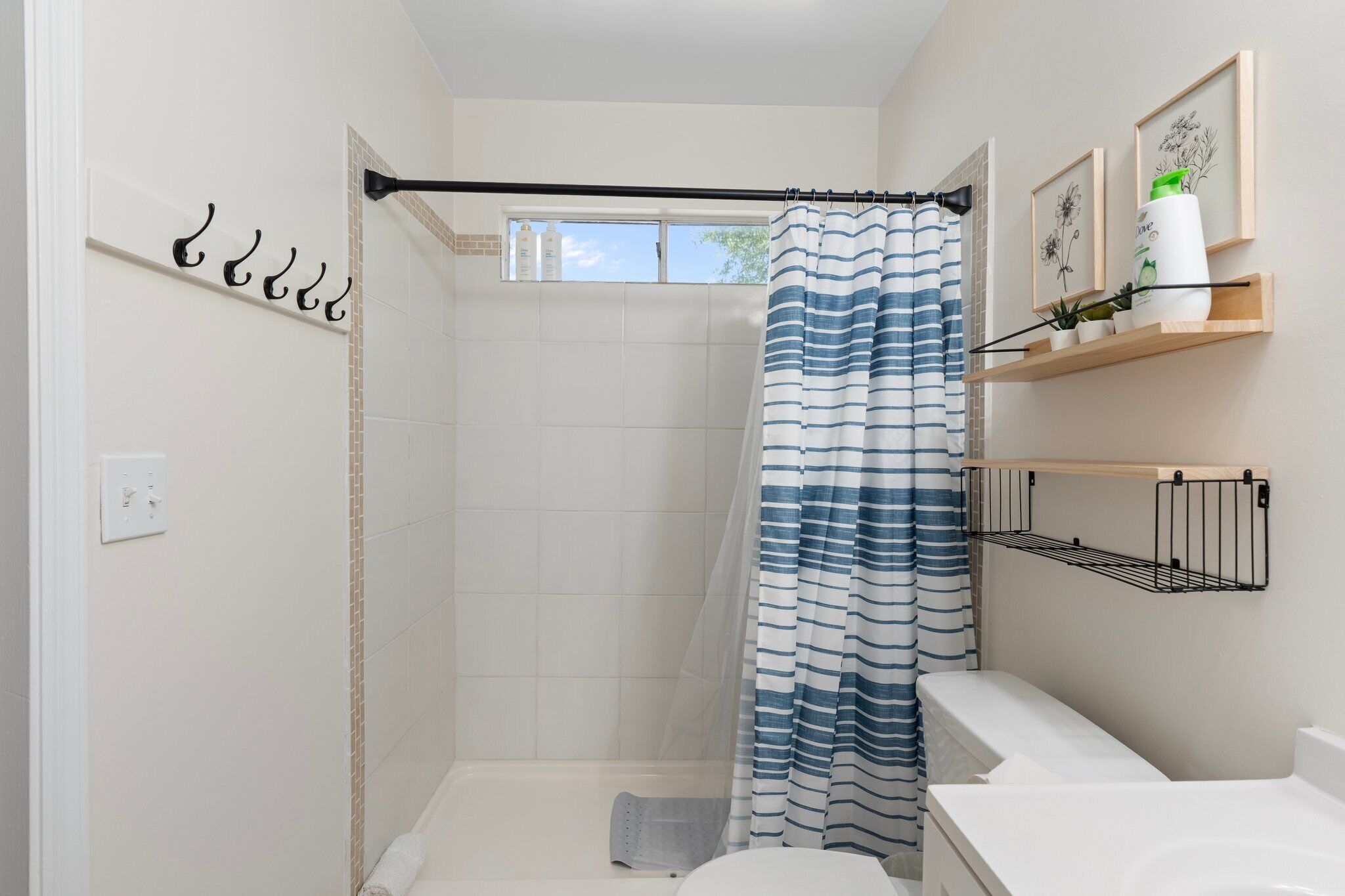 Eine Dusche mit gestreifter Duschvorhang, einem Handtuchhalter, einem Fenster und einem Ablagebereich für Toilettenartikel.
