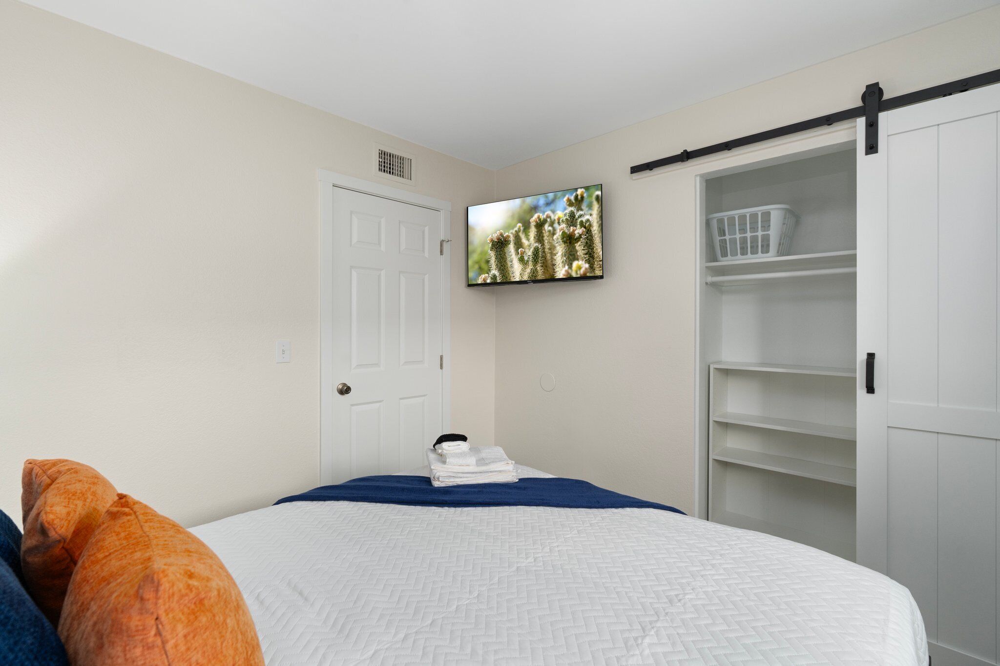 Une chambre à coucher avec un lit, un téléviseur fixé au mur, une porte blanche et une armoire avec une porte coulissante.