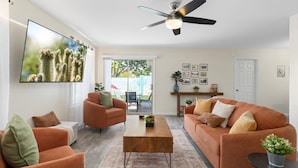 A living room with a ceiling fan, orange sofas, a coffee table, and a TV mounted on the wall. - Button Bungalow (Mesa)