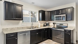 A modern kitchen with dark cabinetry, stainless steel appliances, and a granite countertop. - Button Bungalow (Mesa)