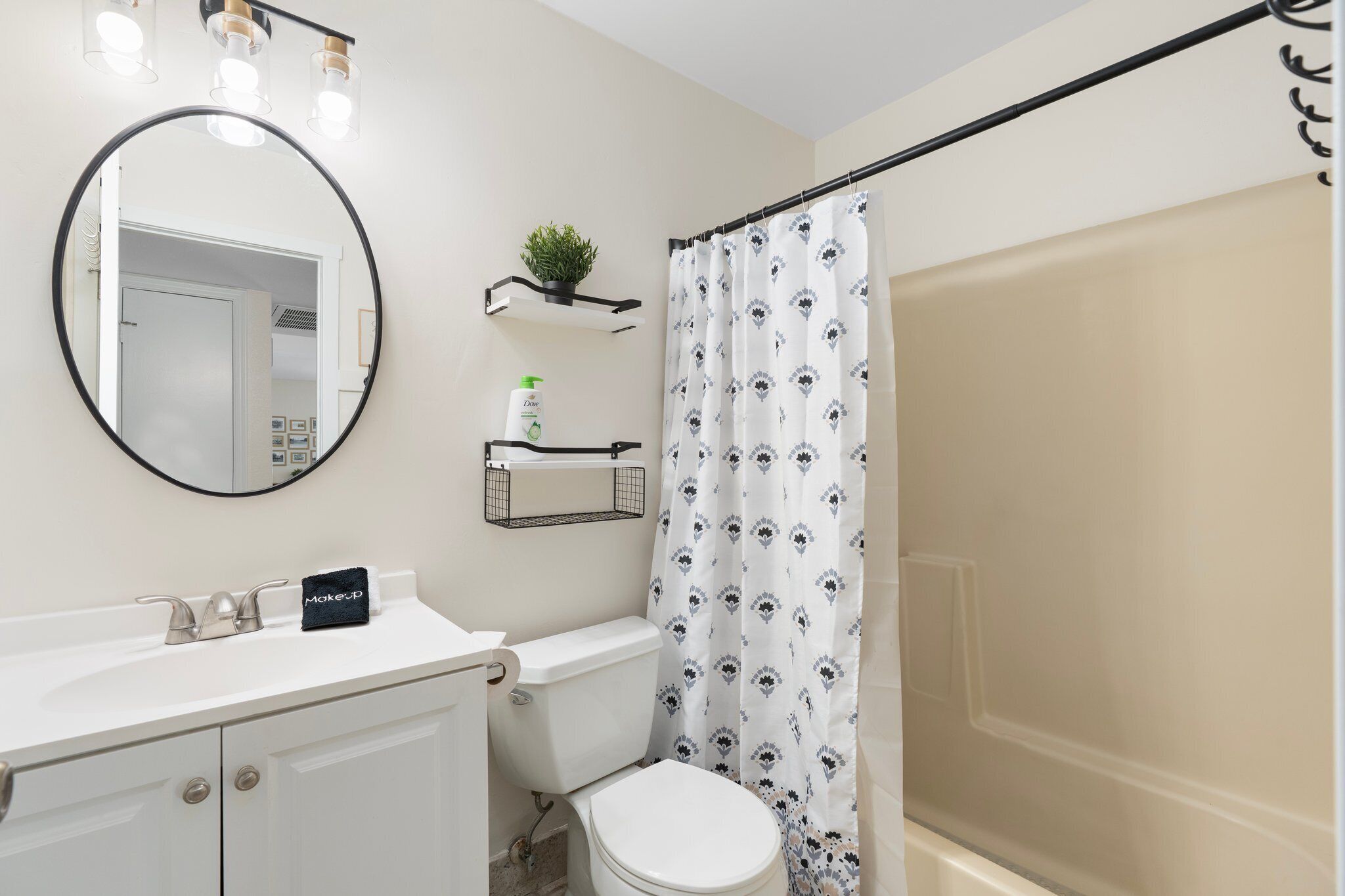 A bathroom with a white sink, a mirror, a toilet, and a shower curtain with a floral pattern.