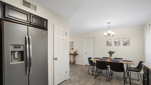 A modern kitchen with a stainless steel refrigerator, a dining table with chairs, and a ceiling light fixture. - Button Bungalow (Mesa)