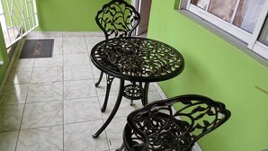 A small patio area with a round metal table and two chairs, a metal gate, and a window with blinds.
