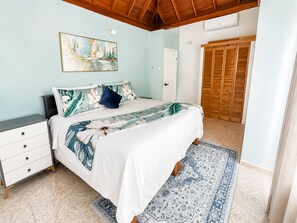A bedroom with a bed, a nightstand, a dresser, a painting on the wall, a wooden ceiling, and a door.