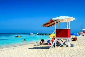 A beach with a lifeguard tower, clear blue water, and a pier in the background. - Charming 2-bedroom apartment in lovely Montego Bay with King Bed, WiFi, AC (Montego Bay)