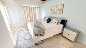 Ein Schlafzimmer mit Bett, Nachttisch, Schubladen, Teppich, Vorhängen und einem Bild an der Wand.