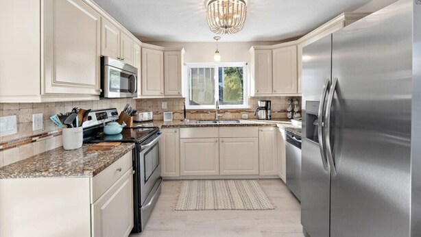 A modern kitchen with stainless steel appliances, light-colored cabinetry, and a large window providing natural light. - Charming Cottage Close to Kemah Boardwalk (Kemah Area)
