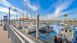 A marina with boats docked, a wooden walkway, and a clear blue sky. - Charming Cottage Close to Kemah Boardwalk (Kemah Area)