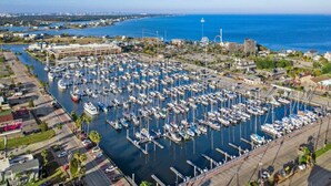 An aerial view of a marina with numerous boats docked, a lighthouse, and a coastal town in the background. - Charming Cottage Close to Kemah Boardwalk (Kemah Area)