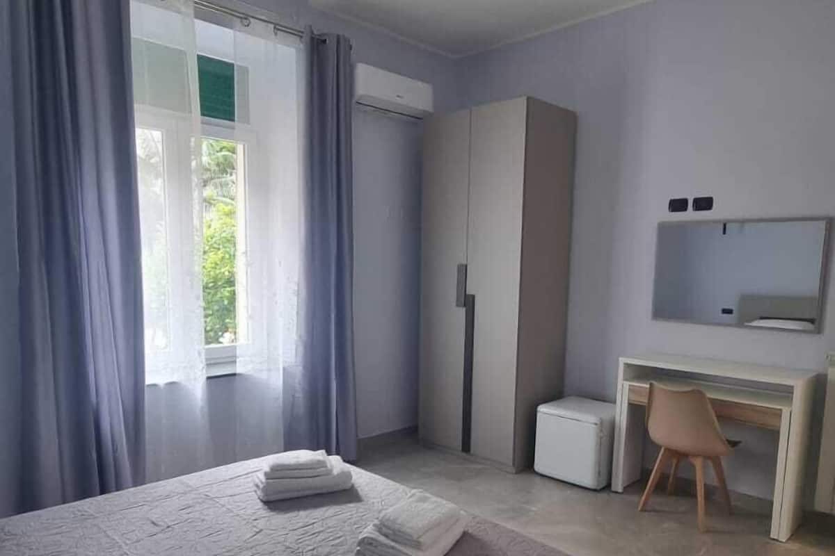 Un dormitorio moderno con una cama grande, un escritorio, un armario y una ventana con cortinas.