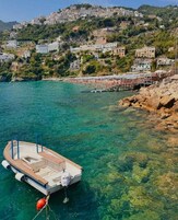 Uma vila costeira com edifícios numa encosta, águas turquesa cristalinas e um barco atracado.