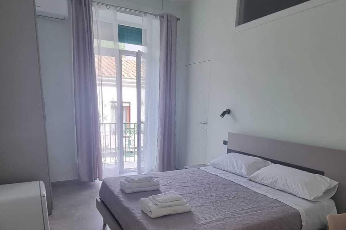 Un dormitorio moderno con una cama grande, una mesita de noche y un ventanal con cortinas.