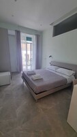 Quarto moderno com uma cama grande, mesa de cabeceira e janela com cortinas.