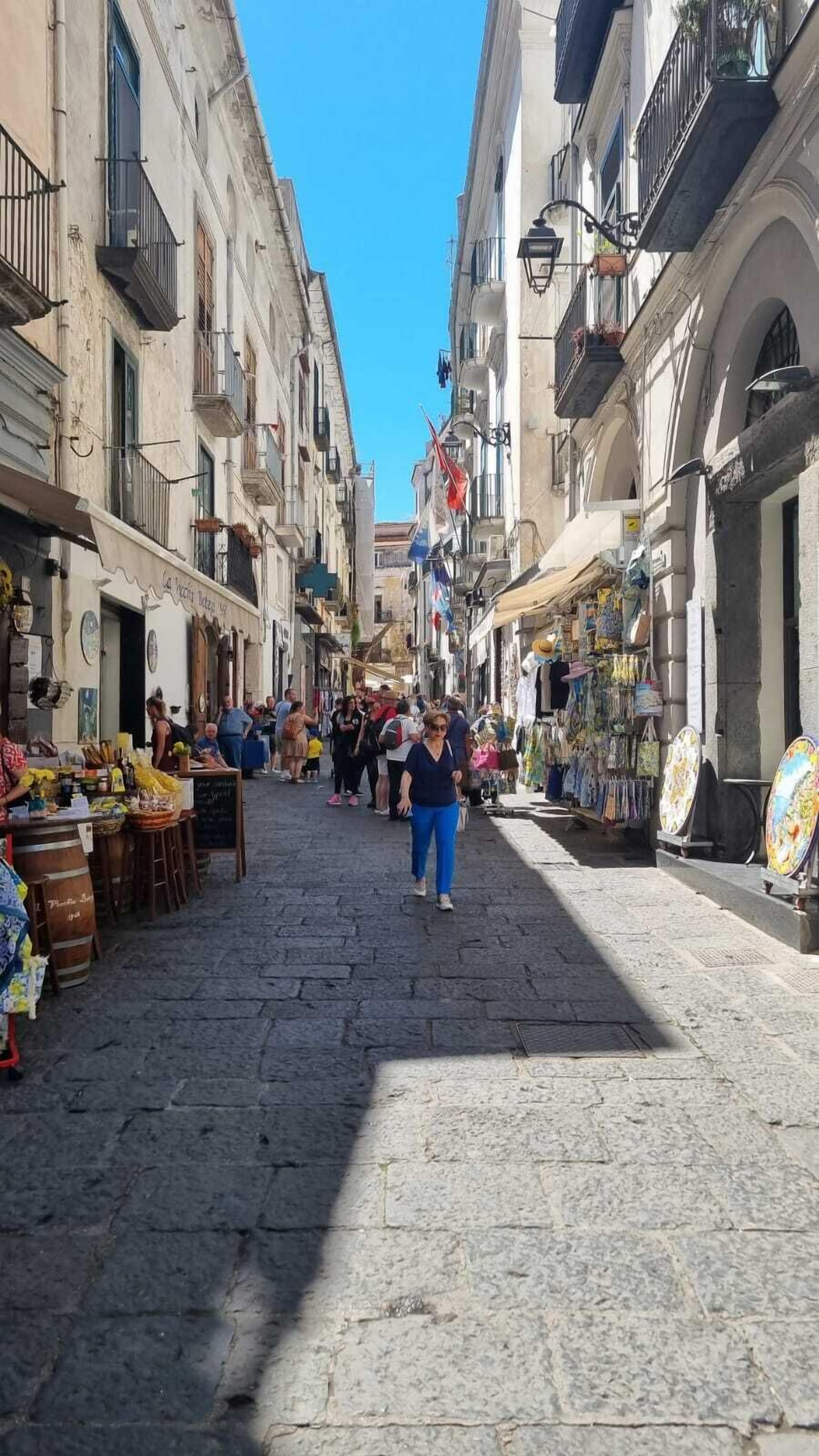 A cobblestone street lined with buildings, some with balconies and outdoor seating areas.